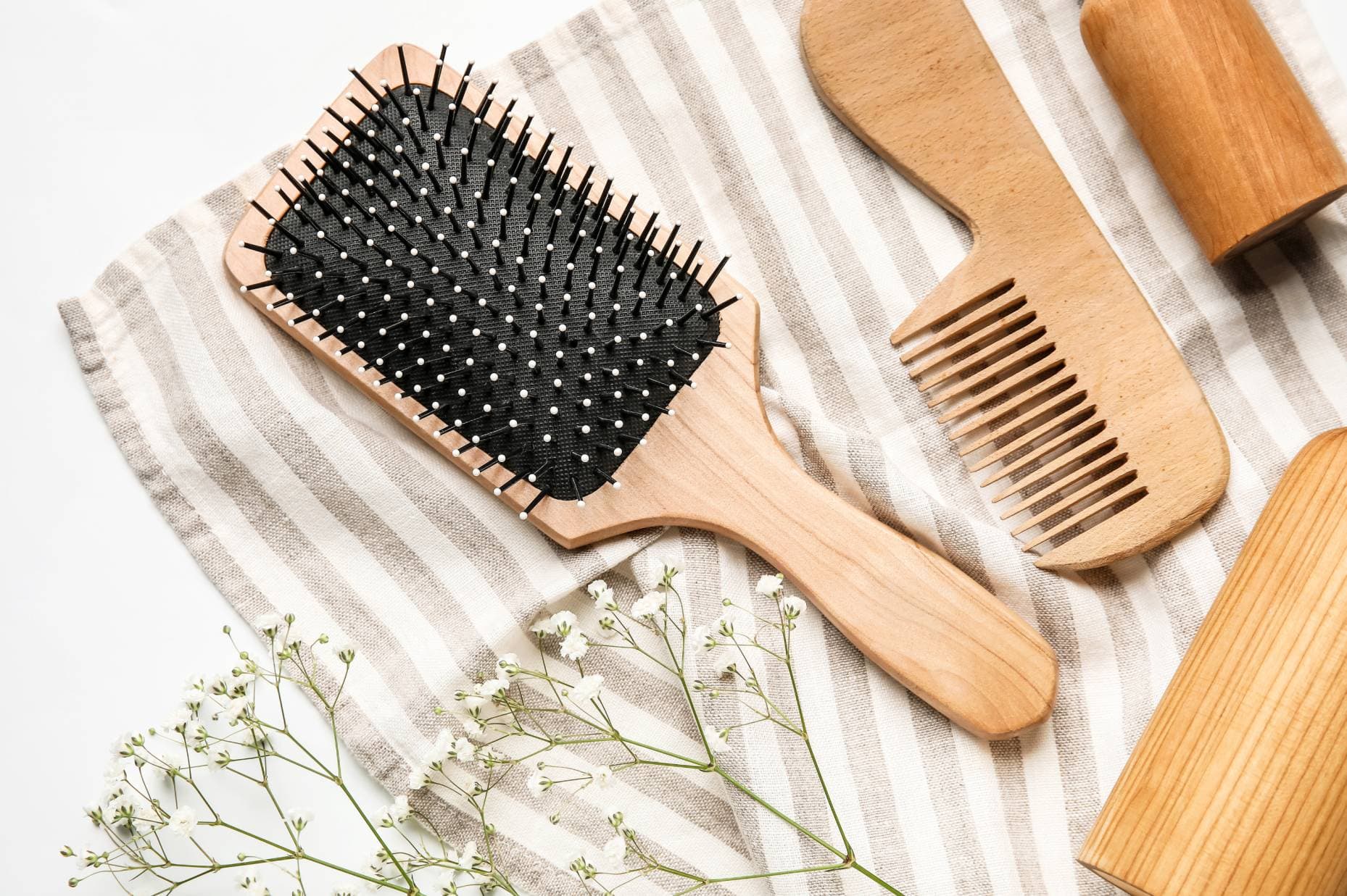 Bamboo hairbrush and comb flat lay with flowers on striped cloth